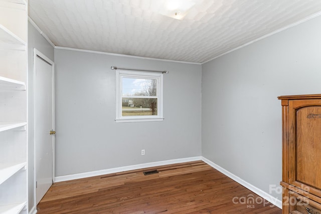 empty room featuring ornamental molding, baseboards, wood finished floors, and visible vents