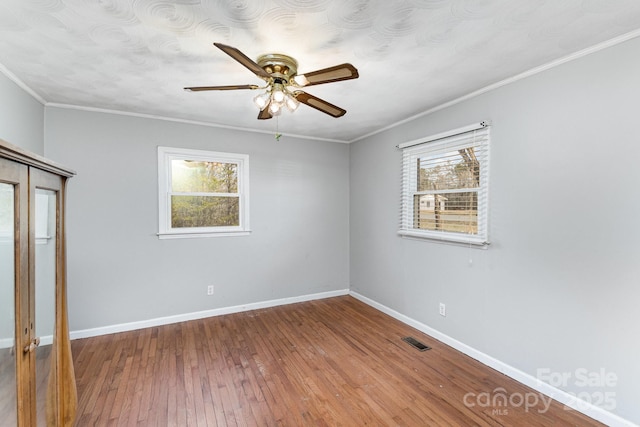 unfurnished bedroom featuring multiple windows, baseboards, wood finished floors, and visible vents