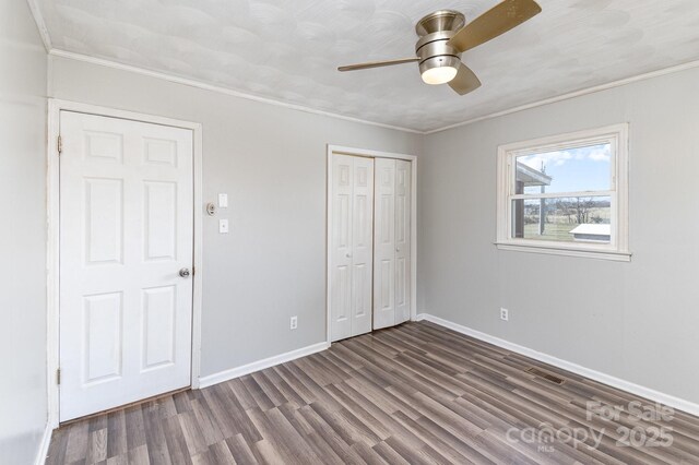 unfurnished bedroom with a closet, dark wood-type flooring, ornamental molding, baseboards, and visible vents