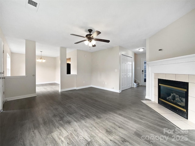 unfurnished living room with a tiled fireplace, ceiling fan with notable chandelier, and wood-type flooring