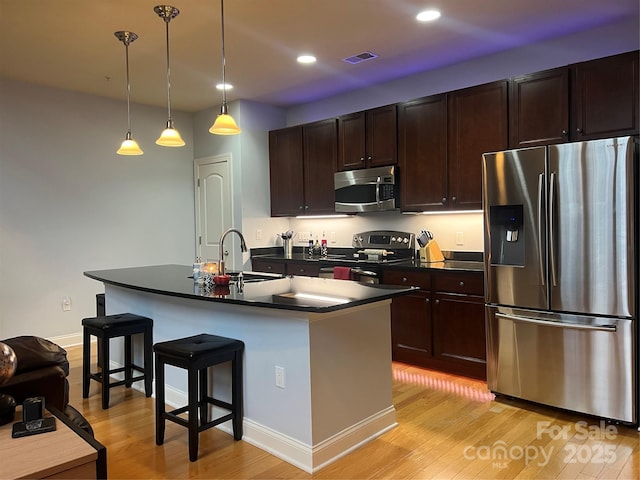 kitchen featuring sink, appliances with stainless steel finishes, hanging light fixtures, a center island with sink, and a kitchen bar