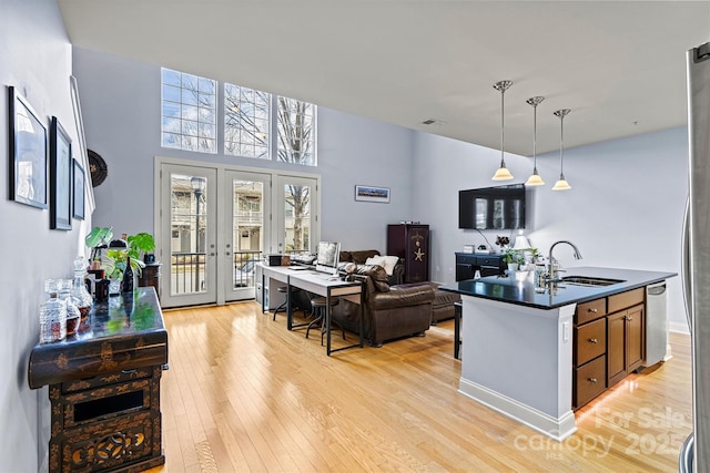 kitchen featuring light wood finished floors, dark countertops, hanging light fixtures, french doors, and a sink