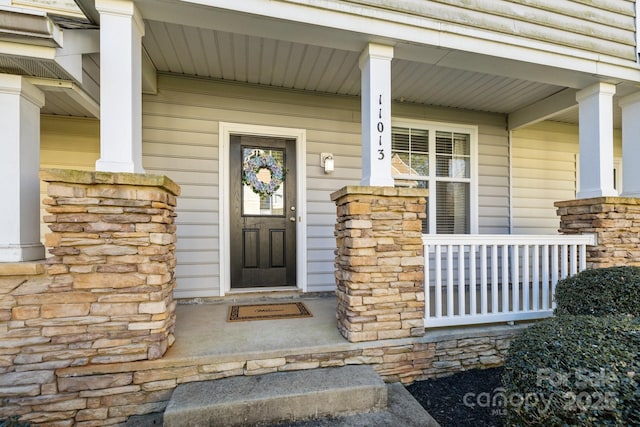 view of exterior entry featuring stone siding and covered porch