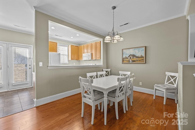 dining area with baseboards, light wood-type flooring, visible vents, and crown molding