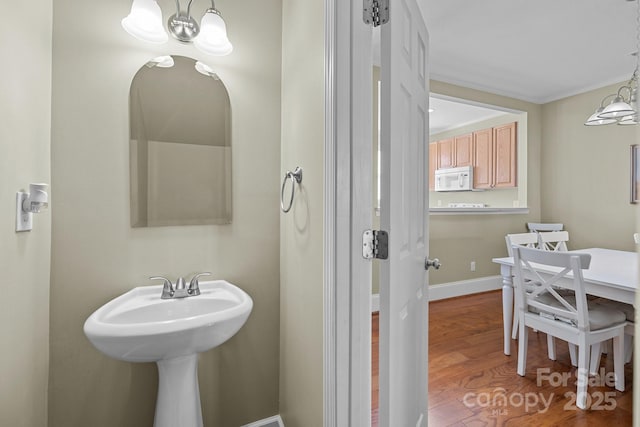 bathroom featuring ornamental molding, a notable chandelier, baseboards, and wood finished floors