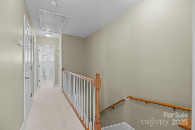 corridor with attic access, baseboards, light carpet, and an upstairs landing