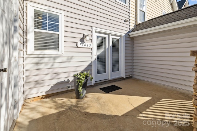 entrance to property featuring roof with shingles and a patio