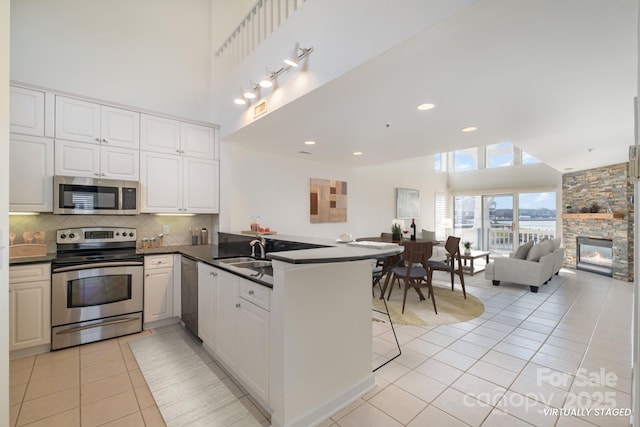 kitchen with stainless steel appliances, a peninsula, white cabinetry, open floor plan, and dark countertops