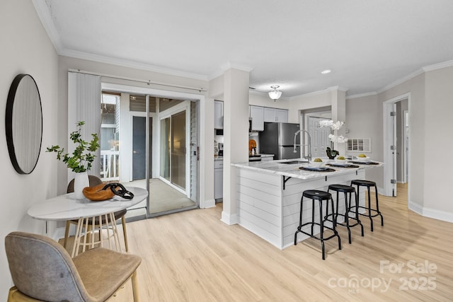 kitchen featuring crown molding, a kitchen bar, stainless steel fridge, and light wood-type flooring