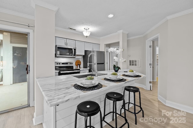 kitchen featuring a breakfast bar, appliances with stainless steel finishes, ornamental molding, light stone countertops, and light wood-type flooring