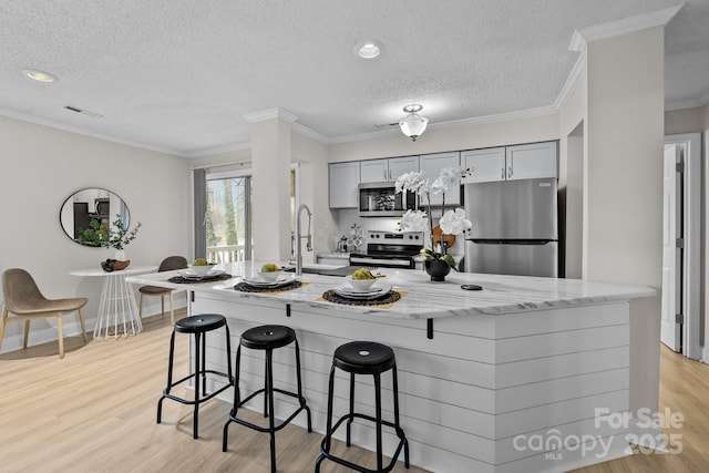 kitchen with sink, gray cabinetry, ornamental molding, stainless steel appliances, and light hardwood / wood-style flooring