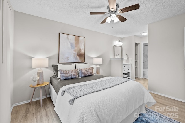 bedroom with ceiling fan, ensuite bath, light hardwood / wood-style floors, and a textured ceiling