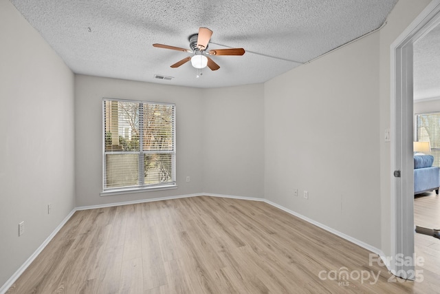 empty room featuring ceiling fan, a wealth of natural light, a textured ceiling, and light hardwood / wood-style floors