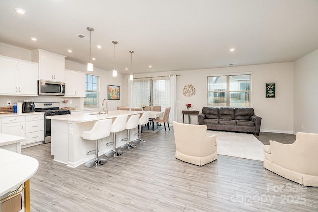 kitchen featuring pendant lighting, white cabinets, a kitchen breakfast bar, stainless steel appliances, and a center island with sink