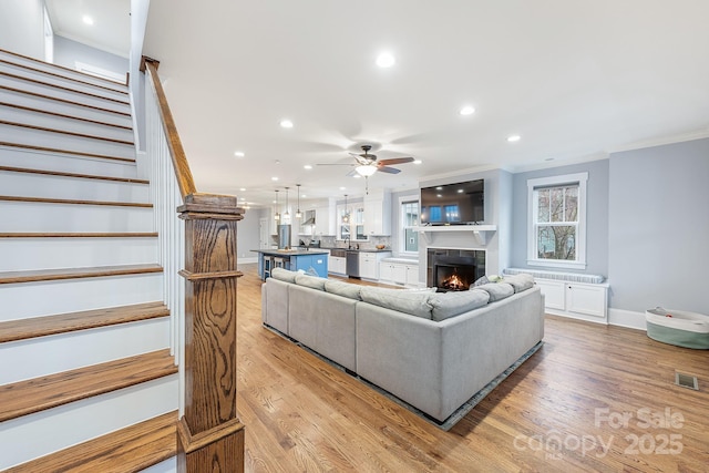 living room with ornamental molding, ceiling fan, and light wood-type flooring