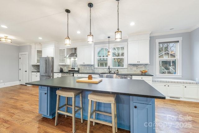 kitchen featuring appliances with stainless steel finishes, a center island, wall chimney range hood, and white cabinets