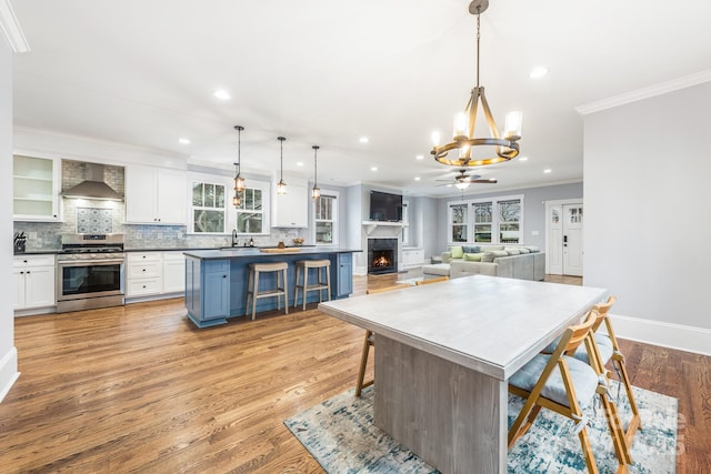 kitchen featuring wall chimney range hood, stainless steel gas range oven, white cabinets, a kitchen island, and decorative light fixtures