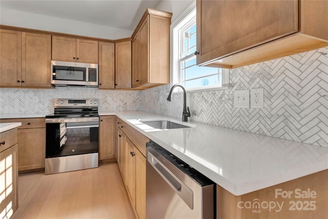 kitchen featuring stainless steel appliances, a sink, light countertops, backsplash, and light wood finished floors