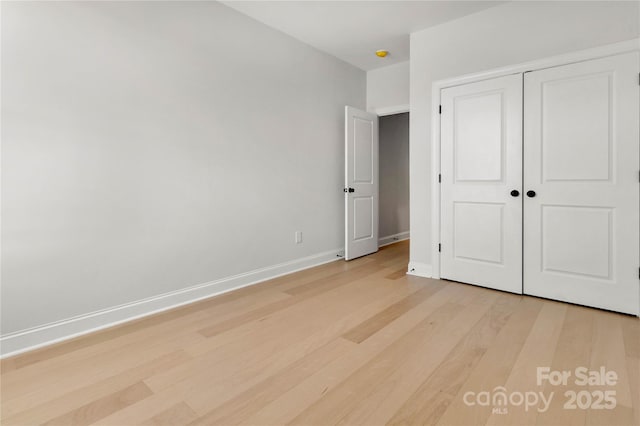 unfurnished bedroom featuring light wood-style floors, baseboards, and a closet