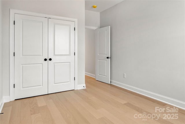 unfurnished bedroom featuring light wood-type flooring, a closet, and baseboards