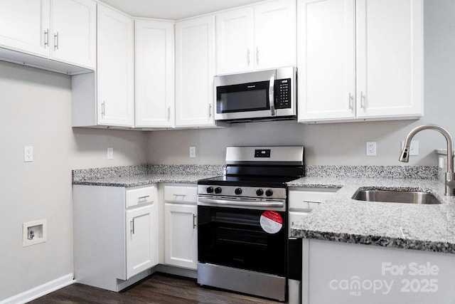 kitchen with stainless steel appliances, a sink, white cabinets, light stone countertops, and dark wood finished floors