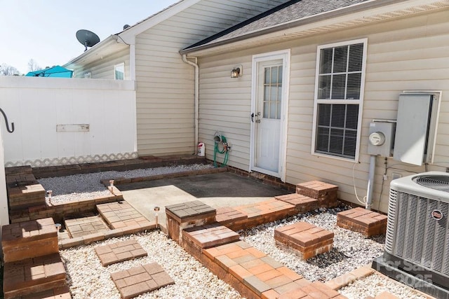 view of exterior entry with roof with shingles, a patio area, fence, and central air condition unit