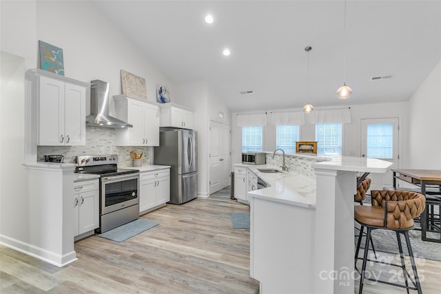 kitchen with sink, appliances with stainless steel finishes, white cabinetry, hanging light fixtures, and wall chimney exhaust hood