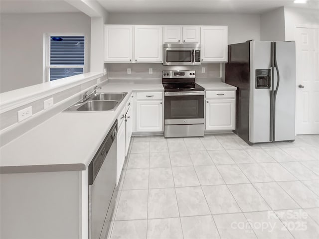 kitchen featuring stainless steel appliances, light countertops, white cabinets, a sink, and a peninsula