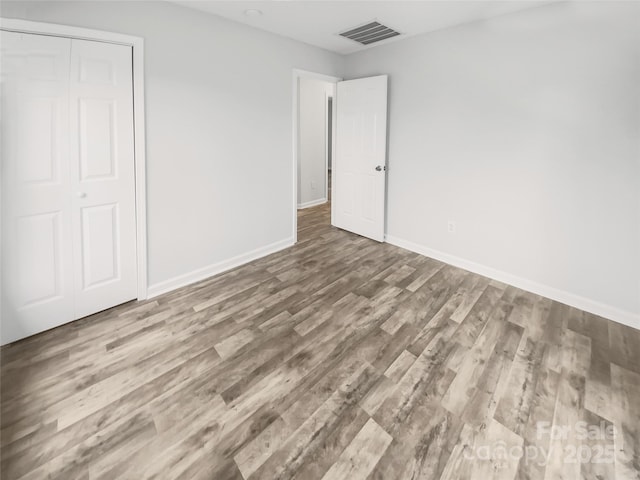 unfurnished bedroom with baseboards, a closet, visible vents, and wood finished floors