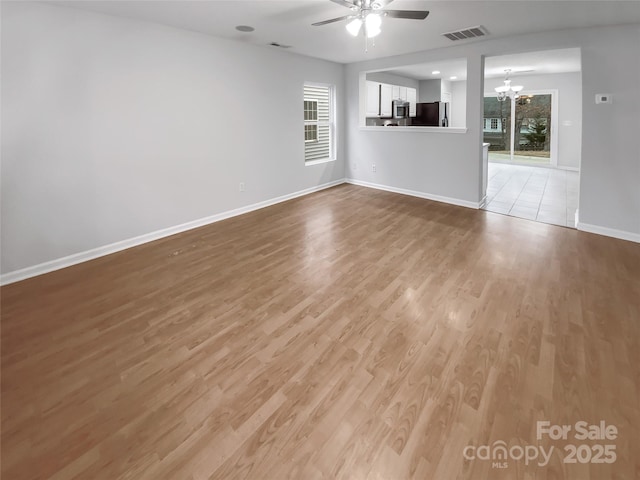 unfurnished living room featuring baseboards, visible vents, light wood finished floors, and ceiling fan with notable chandelier