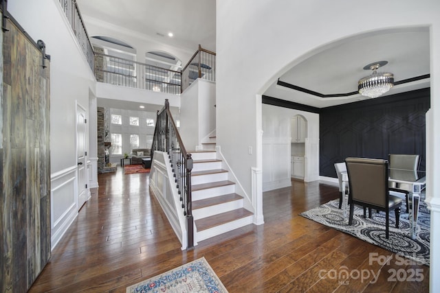 entryway with a decorative wall, stairway, an inviting chandelier, dark wood-type flooring, and a barn door