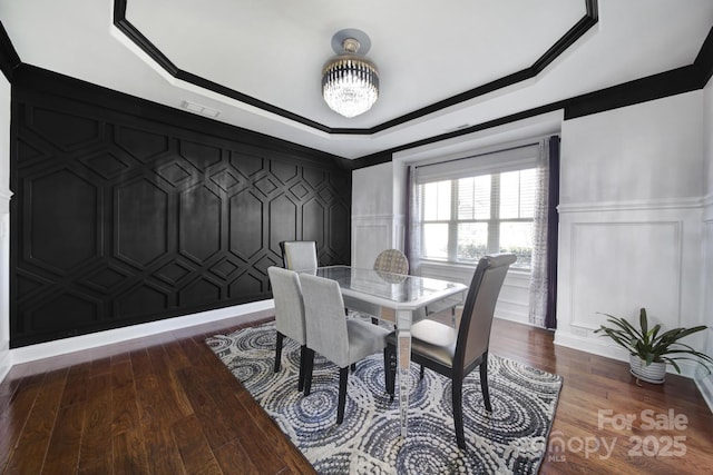 dining area with a raised ceiling, visible vents, a decorative wall, and wood finished floors