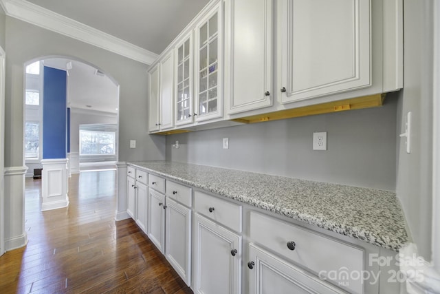 kitchen featuring arched walkways, light stone countertops, glass insert cabinets, and white cabinetry