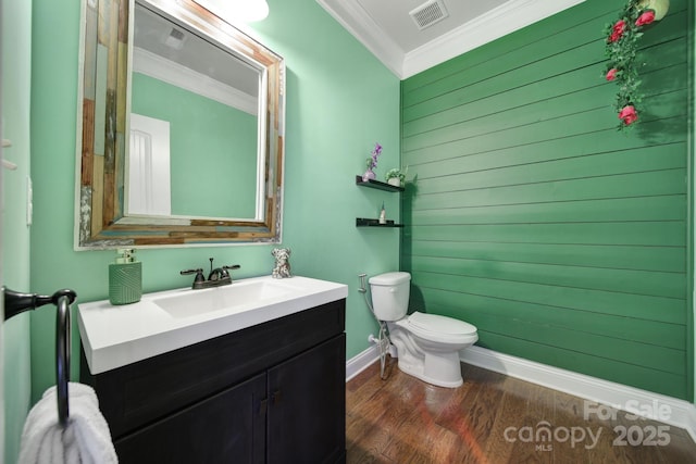 half bath featuring visible vents, toilet, wood finished floors, crown molding, and vanity