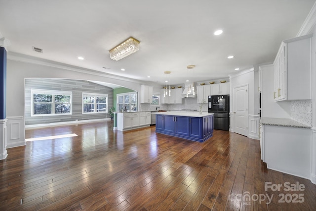 kitchen with a center island, white cabinets, blue cabinetry, and black fridge