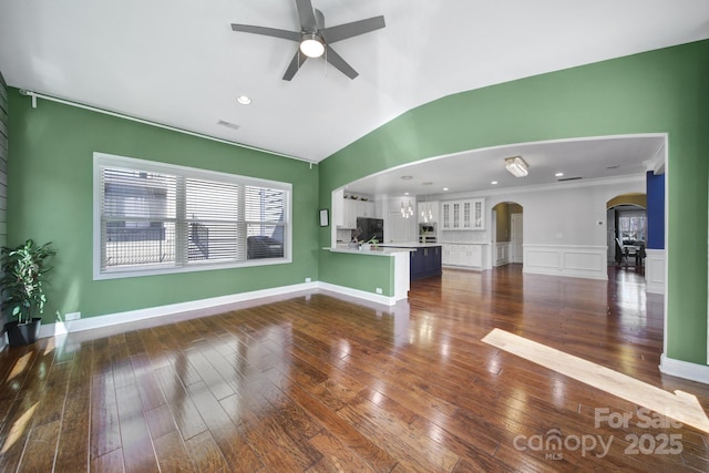 unfurnished living room featuring arched walkways, lofted ceiling, a ceiling fan, wainscoting, and dark wood finished floors