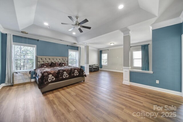 bedroom featuring crown molding, decorative columns, a raised ceiling, wood finished floors, and baseboards