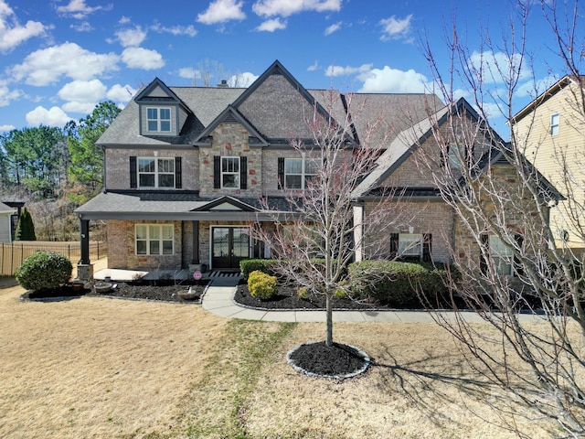 craftsman house with covered porch, a front lawn, fence, and brick siding