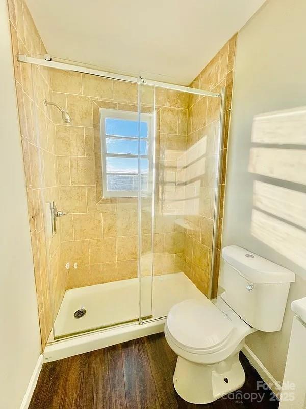 bathroom with a shower with door, toilet, and hardwood / wood-style floors