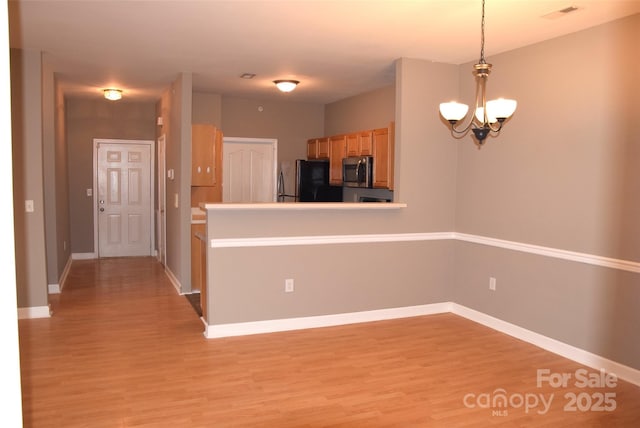 kitchen featuring stainless steel microwave, freestanding refrigerator, decorative light fixtures, light wood-style floors, and a chandelier