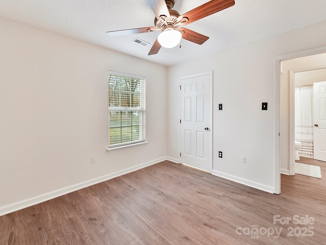 spare room with a textured ceiling, light wood-style flooring, visible vents, and baseboards