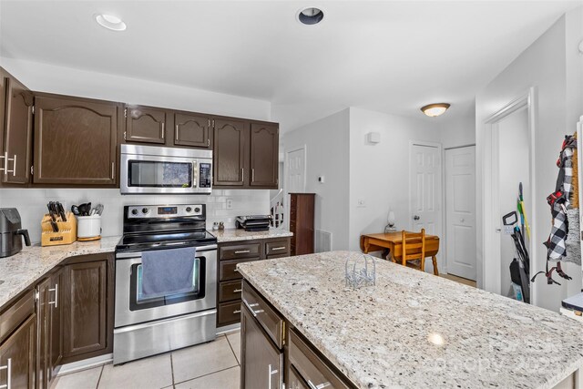 kitchen featuring light tile patterned floors, light stone countertops, stainless steel appliances, decorative backsplash, and dark brown cabinets