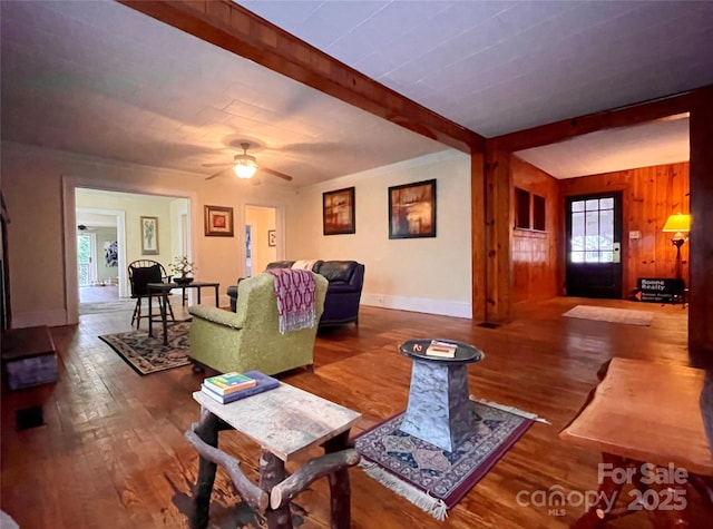 living room with hardwood / wood-style floors, ceiling fan, beamed ceiling, and wood walls