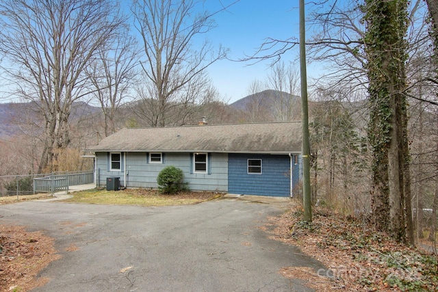 exterior space featuring cooling unit, roof with shingles, driveway, and fence