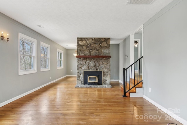 unfurnished living room featuring wood finished floors, baseboards, visible vents, stairs, and a textured ceiling