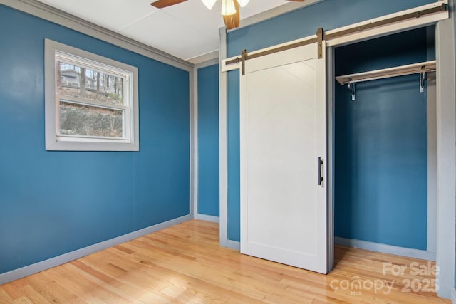 unfurnished bedroom featuring a barn door, wood finished floors, baseboards, and a closet