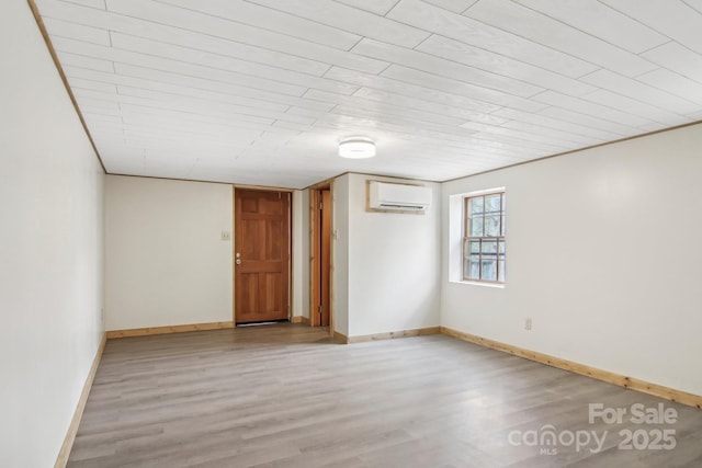 spare room featuring light wood-style flooring, a wall mounted AC, and baseboards