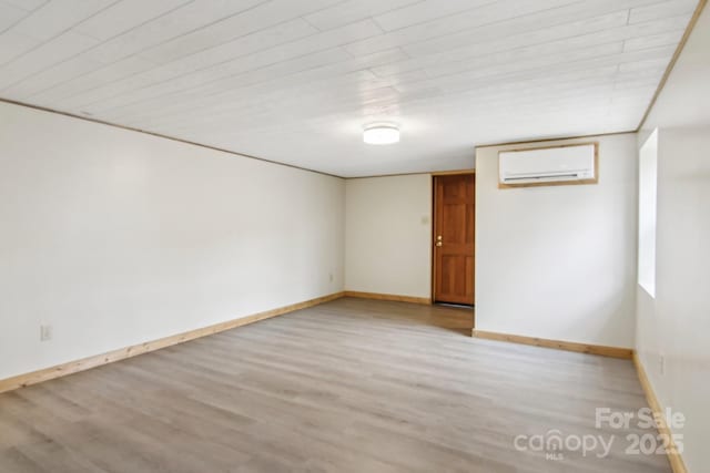 spare room featuring baseboards, an AC wall unit, and wood finished floors