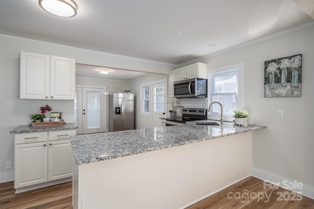 kitchen with a peninsula, light stone countertops, appliances with stainless steel finishes, and a sink