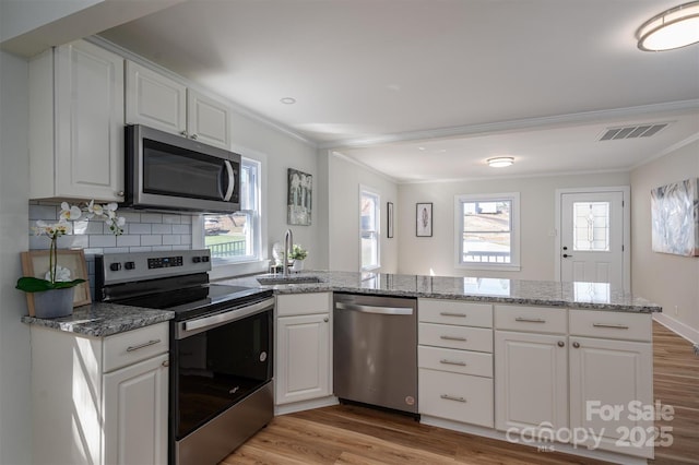 kitchen with a peninsula, a sink, visible vents, appliances with stainless steel finishes, and light wood-type flooring